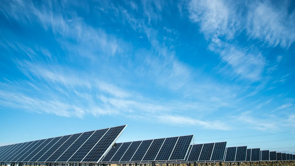 Fileiras de painéis solares inclinados sob céu azul com nuvens finas