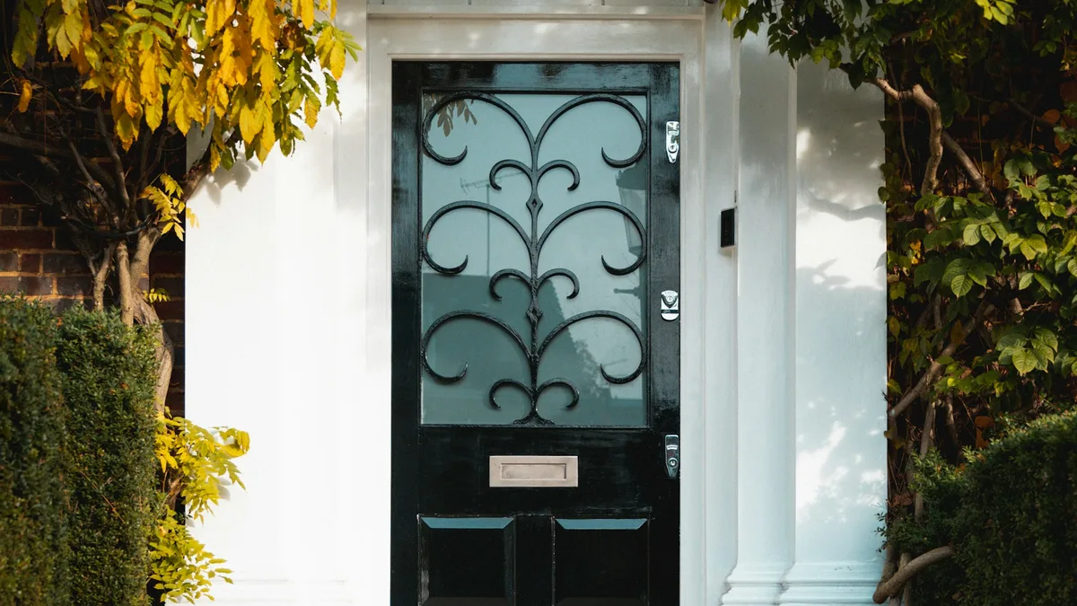 Porta de entrada preta com vidro decorado em uma casa branca com árvores