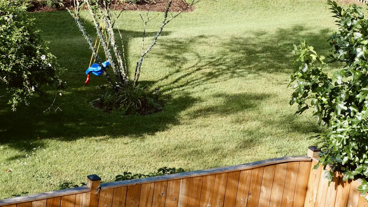 Quintal gramado com cerca de madeira e arbustos ao sol, área típica para uma câmera de segurança sem fio solar