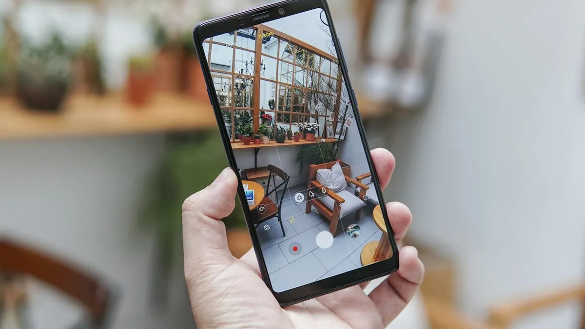 Mão segurando um celular com a imagem de uma câmera de segurança wifi instalada na sala