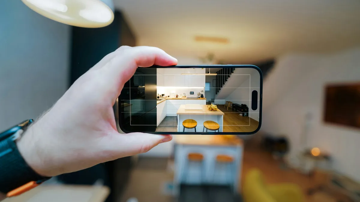 Mão segurando um smartphone que mostra a imagem ao vivo de uma sala, como em uma câmera espiã com Wi-Fi