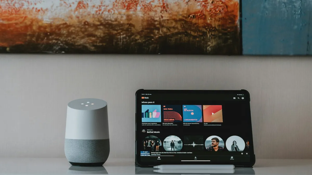 Alto-falante inteligente e tablet sobre uma estante, representando a integração com assistentes de voz