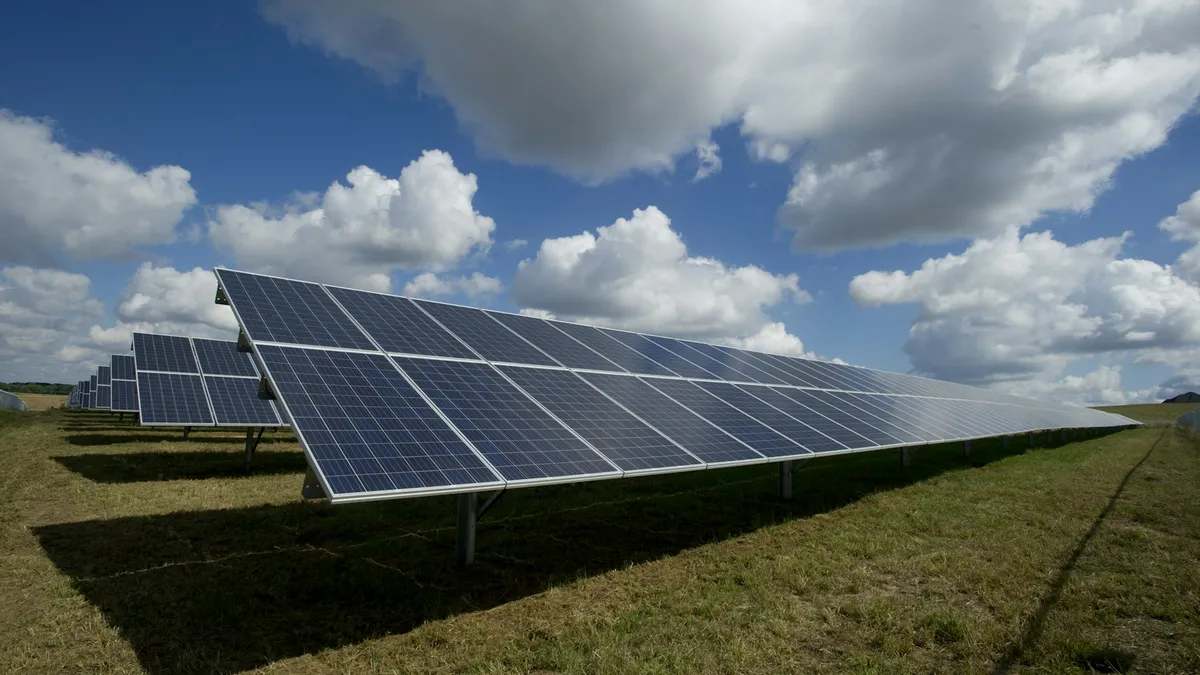 Painéis solares enfileirados em um campo aberto sob céu com nuvens, cenário típico de área rural
