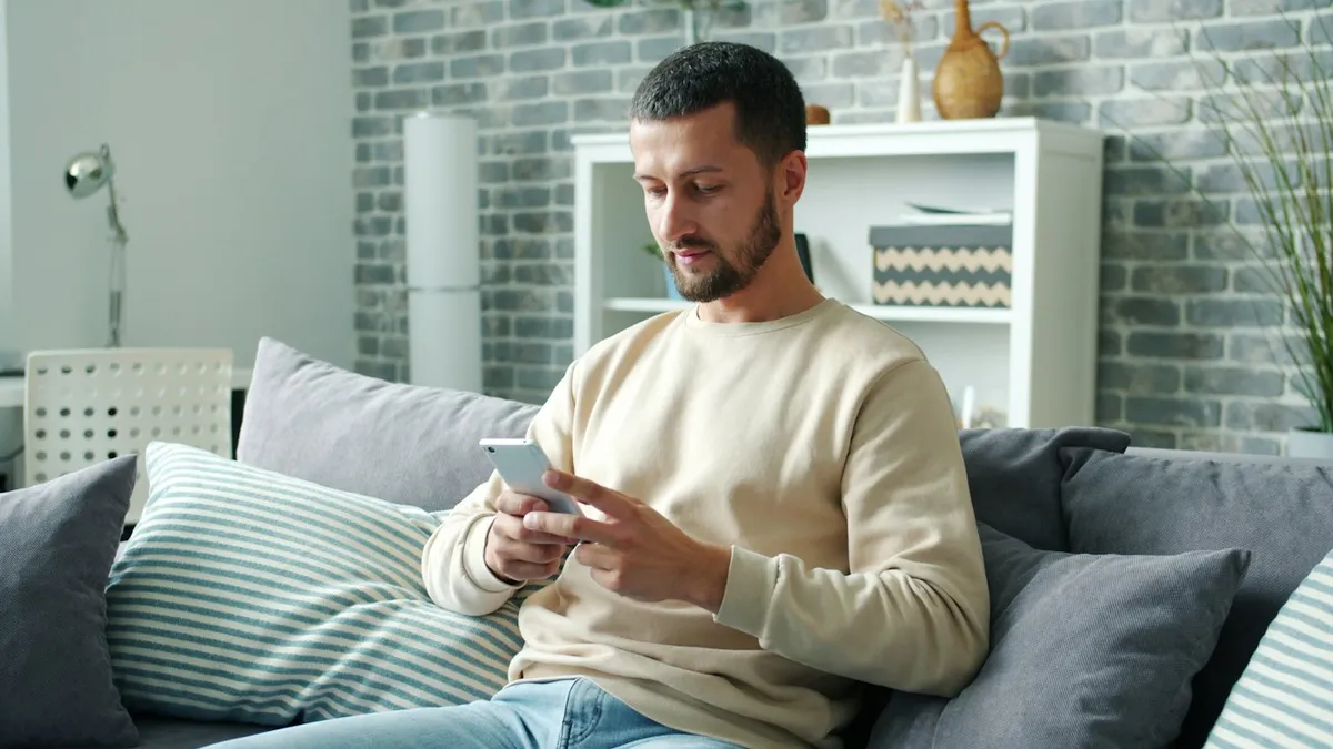 Homem sentado no sofá usando smartphone