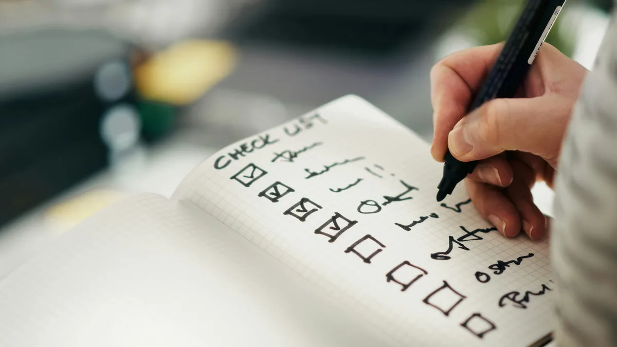 Mão marcando itens em uma lista de verificação em um caderno