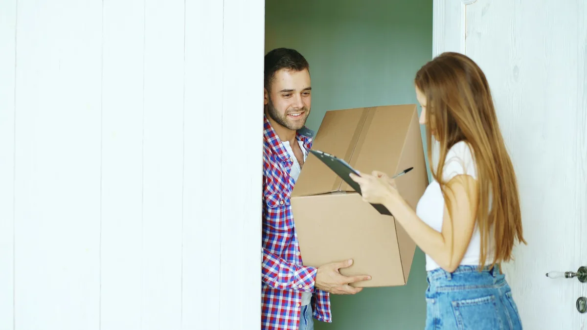 Entregador entregando uma caixa de papelão para uma mulher na porta de casa