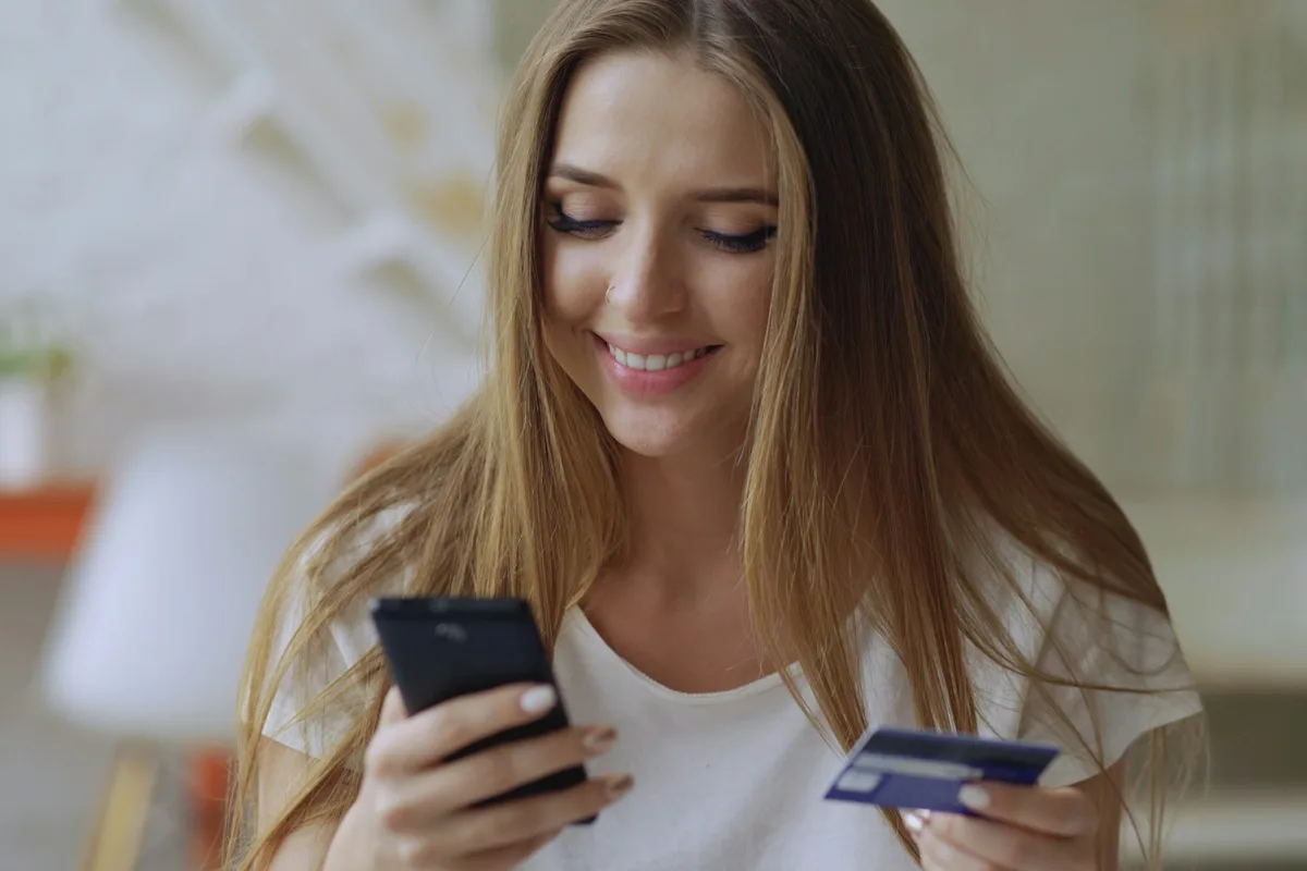 Mulher segurando celular e cartão de crédito para comprar câmera de segurança online