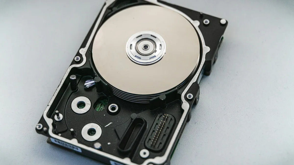 Disco rígido de computador aberto sobre superfície cinza, mostrando o prato e a cabeça de leitura