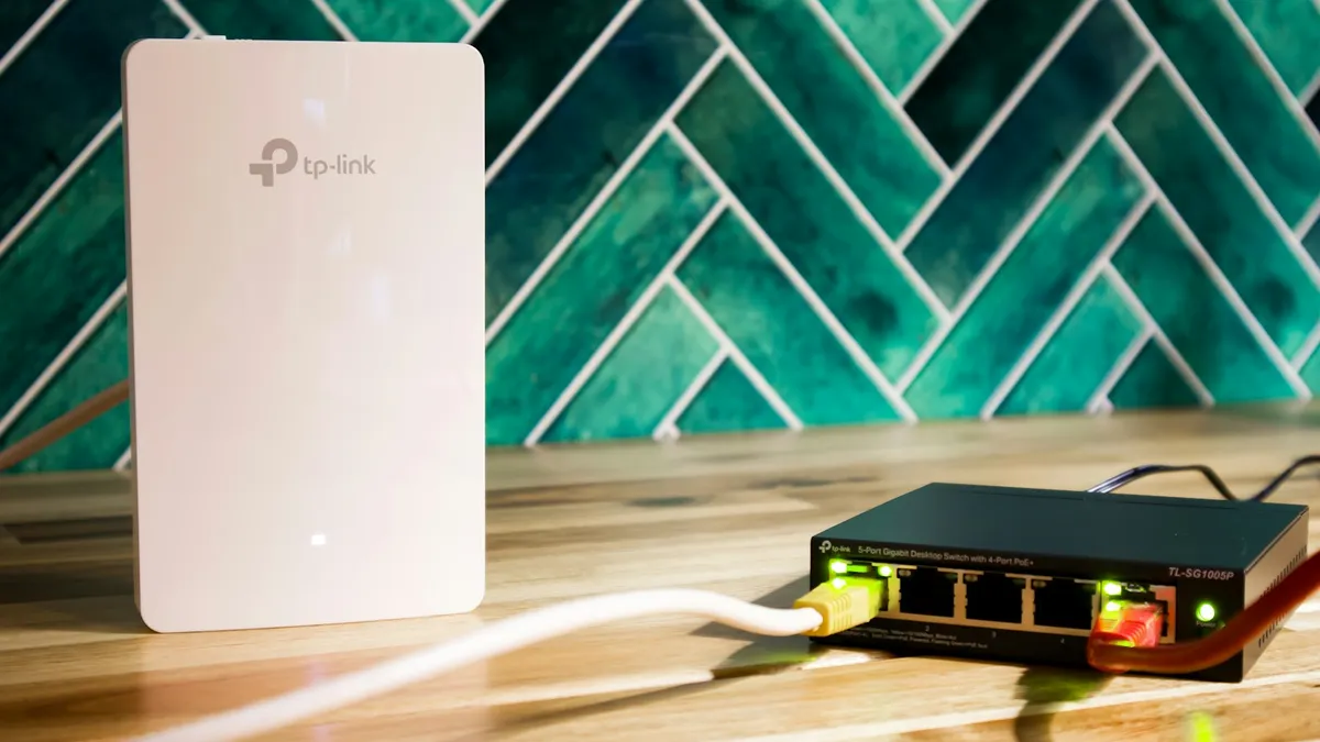 Roteador Wi-Fi branco e switch de rede com cabos conectados sobre mesa de madeira