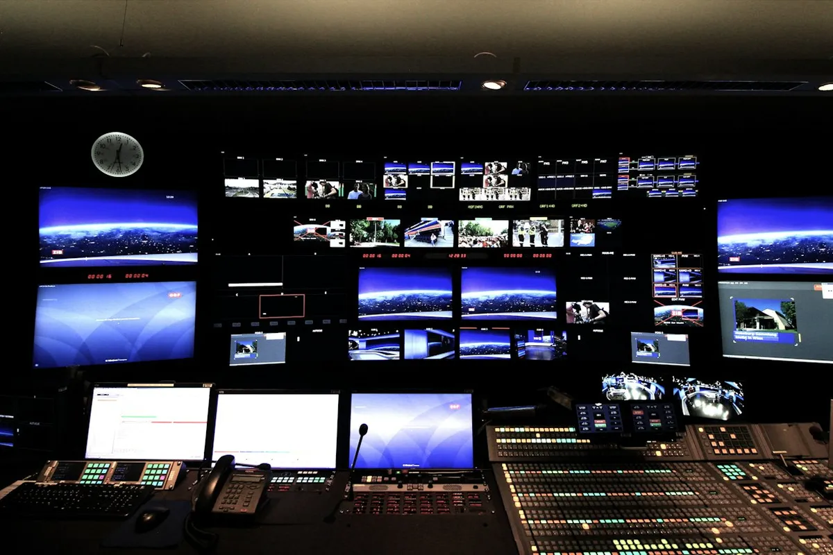 Sala de controle escura com vários monitores exibindo imagens de câmeras de segurança