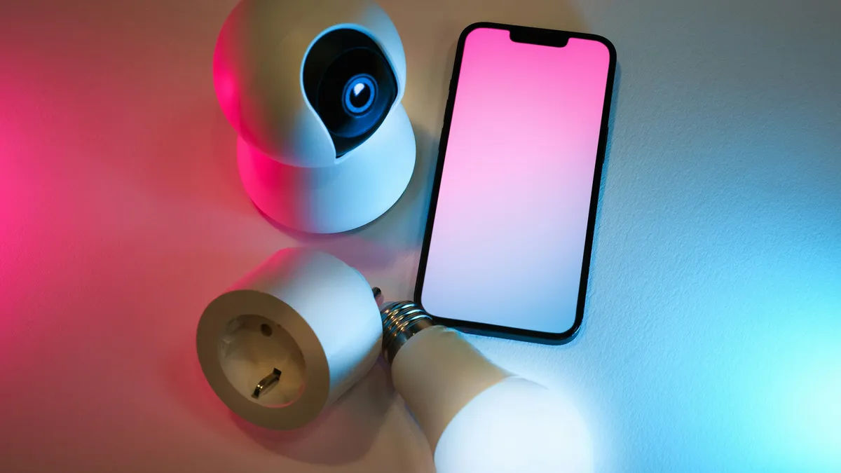 Câmera, tomada inteligente e celular sobre uma mesa, dispositivos conectados que se integram a um kit alarme residencial com aplicativo