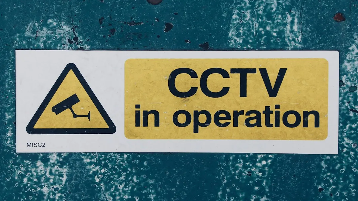 Placa de aviso de CCTV em operação presa em parede azulada