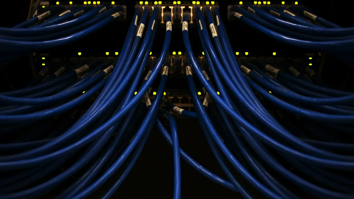 Cabos de rede azuis ligados a um painel em um rack de equipamentos