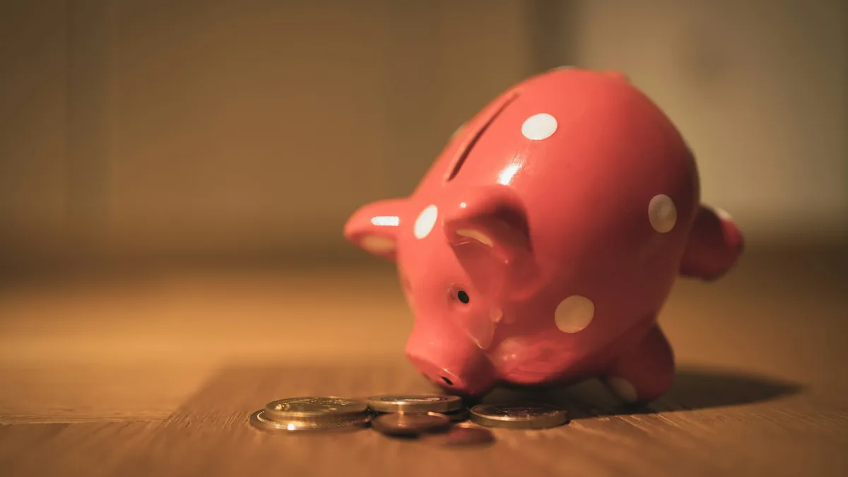 Cofrinho rosa com bolinhas brancas ao lado de moedas sobre uma mesa de madeira