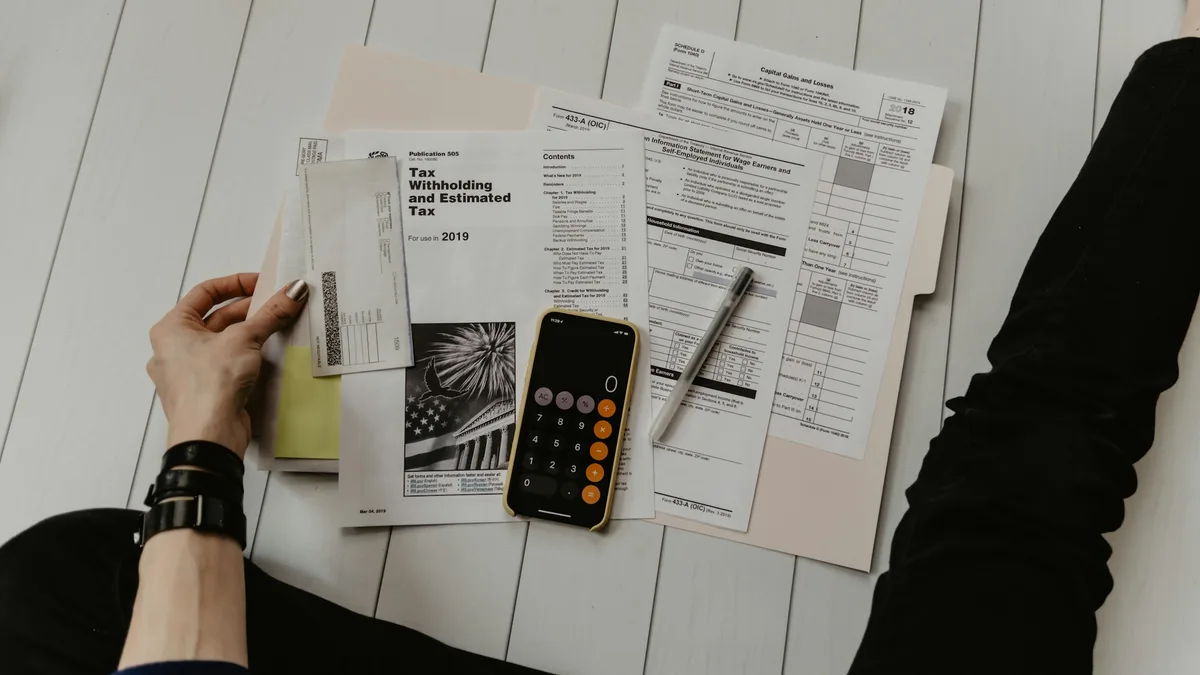 Pessoa somando contas e documentos ao lado de celular com calculadora aberta