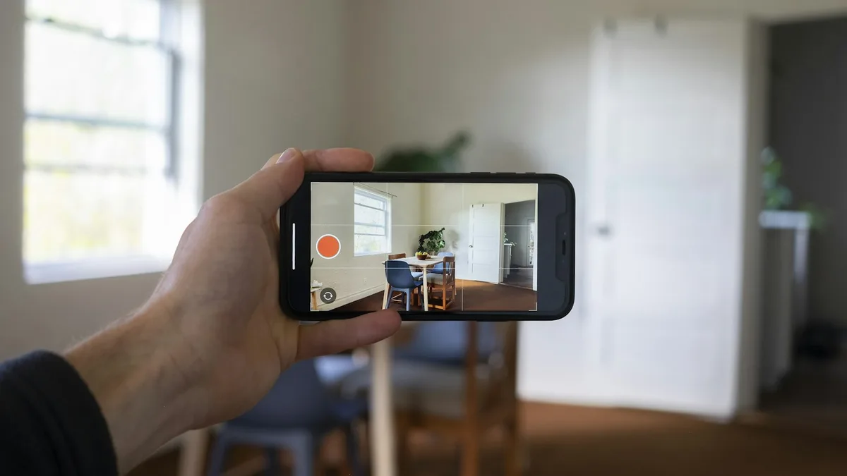 Mão segurando um celular que mostra a imagem de uma câmera de segurança interna em tempo real