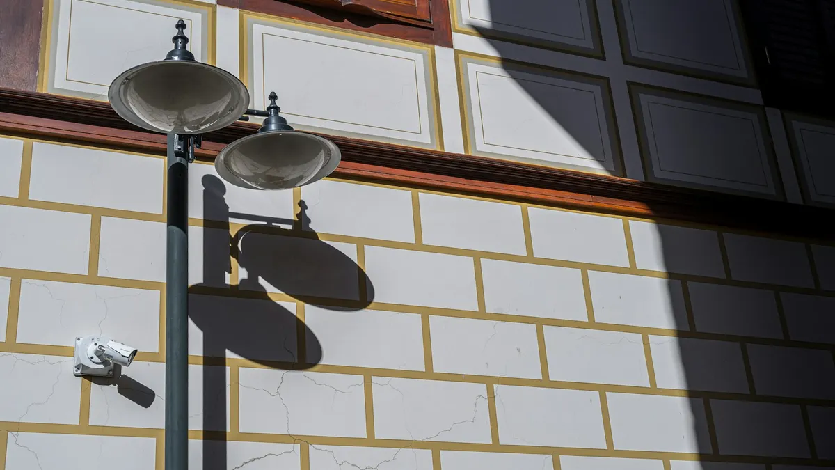 Câmera de segurança pequena fixada na fachada de um prédio, ao lado de um poste