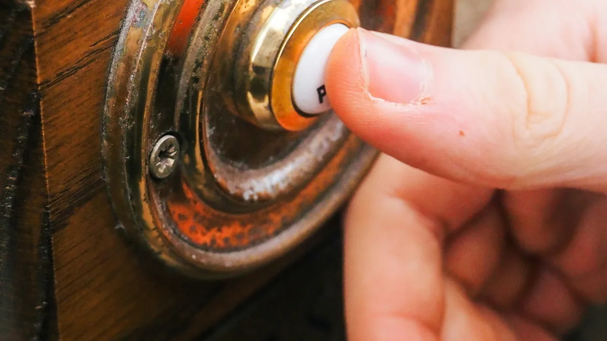 Mão apertando botão de campainha antiga de latão em porta de madeira