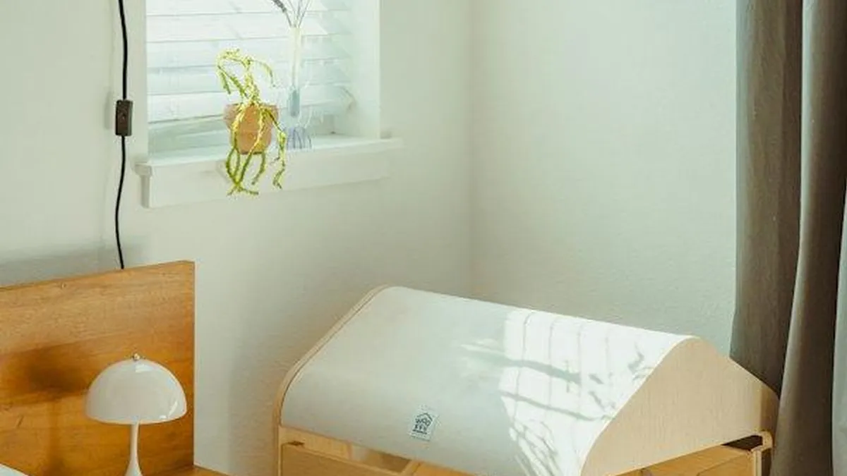Quarto de bebê com berço de madeira clara, cama e janela, ambiente típico para uma câmera interna